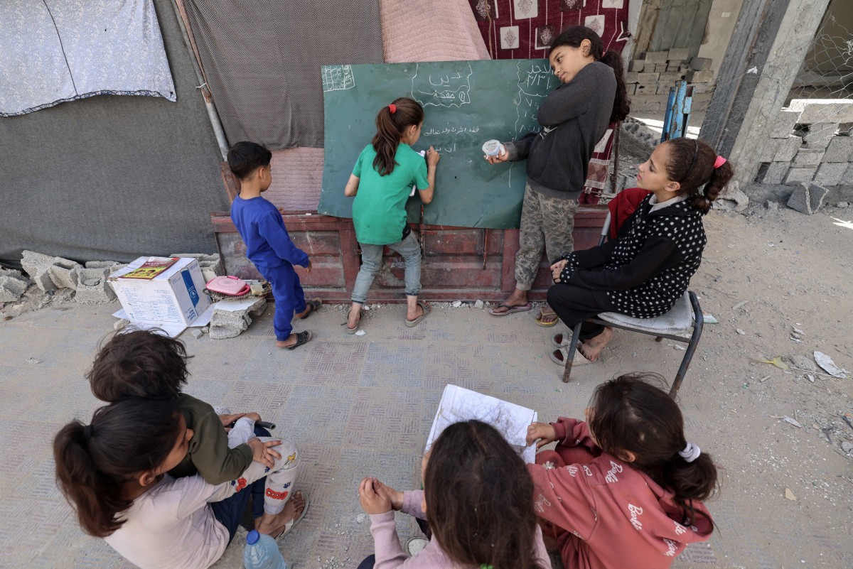 A displaced Palestinian girl writes on a chalkboard as children look on in Rafah in the southern Gaza Strip on March 31, 2024, amid the ongoing conflict between Israel and the militant group Hamas. (Photo by MOHAMMED ABED / AFP)
