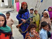 In this photograph taken on April 22, 2019, Afghan woman Niaz Bibi (C in blue),70, holds a weapon as she stands among her orphaned children and grandchildren at their home in the Kot district of the Nangarhar province. NOORULLAH SHIRZADA / AFP