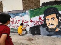 A child watches as a local artist works on a mural painting showing the late Syrian rebel fighter Abdel-Basset al-Sarout in the town of Binnish in the jihadist-held northern Idlib province on June 8, 2019. OMAR HAJ KADOUR / AFP