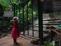 This picture taken on June 13, 2019 shows a girl looking through a gate at the entrance of the Tham Luang cave, in which 12 boys from the "Wild Boars" football team and their coach were trapped last year, in the Mae Sai district of Chiang Rai province. Lillian SUWANRUMPHA / AFP