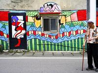 This picture taken on March 30, 2019 shows a local resident walking past a wall painted by Hakka graffiti artist Wu Tsun-hsien in the Taiwanese village of Ruan Chiao. Nestled in the mist-covered foothills of Taiwan's central mountain range, Ruan Chiao village is virtually devoid of young people, but artist Wu Tsun-hsien is coaxing the Instagram generation back by transforming local homes into a canvas of colour. Sam YEH / AFP