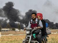 A Syrian couple use a motorcycle to flee the countryside of the northeastern Syrian town of Ras al-Ain on the Turkish border, toward the west to the town of Tal Tamr on October 19, 2019. The smoke behind them is from burning tyres used to impede visibility from warplanes. Delil SOULEIMAN / AFP