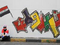 An Iraqi demonstrator clad with the national flag rests in front of a mural which reads "we want a homeland", amid ongoing anti-government protests in the capital Baghdad on November 3, 2019. Protesters in Iraq's capital and the country's south shut down streets and government offices in a new wave of civil disobedience, escalating their month-long movement demanding wholesale change of the political system. AHMAD AL-RUBAYE / AFP
