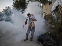 A man holds a boy during clashes with police outside the refugee camp of Moria on the Greek island of Lesbos, on September 29, 2019. At least one migrant died on September 29, 2019, after a fire broke out in Moria, the over-crowded refugee camp on the Greek island of Lesbos, Greece's Health Ministry said. Police were firing tear gas to control crowds who started rioting after the fire ignited inside the camp, according to an AFP correspondent. ANGELOS TZORTZINIS / AFP
