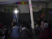 A woman gives evening English lessons to migrants and refugees with a flashlight as they don't have electricity at a makeshift camp next to the camp of Moria in the Greek island of Lesbos on November 29, 2019. ARIS MESSINIS / AFP