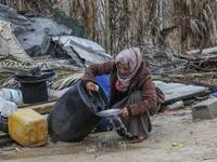 A Palestinian woman carries washes the dishes outside her shack in Khan Yunis in the southern Gaza Strip on January 10, 2020. A family of 17, whose house was destroyed by an Israeli air strike last November, now live in a shack in cold weather and heavy rain. SAID KHATIB / AFP