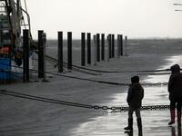 People walk near fish trawlers at the flooded harbor of Wremen, on the North Sea near Bremerhaven, northern Germany, on Febuary 11, 2020. Fierce winds and heavy rains claimed at least six lives across northern Europe on February 11, 2020, as Storm Ciara disrupted travel, grounded hundreds of flights, flooded roads and left vast areas without power. Patrik Stollarz / AFP