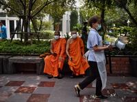 Monks wearing face masks sit outside a temple while a worker carries materials for use to disinfect the Wat Pak Nam Buddhist temple, as part of measures against the COVID-19 novel coronavirus, in Bangkok on March 16, 2020. Lillian SUWANRUMPHA / AFP