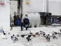A pigeon owner, wearing personal protective equipment, feeds his pigeons on the rooftop of his building in the southern suburb of Beirut on April 11, 2020. ANWAR AMRO / AFP