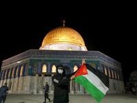 A Palestinian youth waves a national flag in front of the Dome of Rock at the Al-Aqsa Mosque compound, before the start of the dawn prayer (salat al-fajr) inside the compound in Jerusalem's Old City, on May 31, 2020, after a two-month closure due to the COVID-19 pandemic. AHMAD GHARABLI / AFP