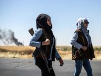 Smoke billows from an oil field as Kurdish female volunteers, from the newly formed Community Protection Forces, guard a wheat field, against threats by jihadists to burn the crops, during harvest season on June 13, 2020, in the countryside east of Qamishli in Syria's northeastern Hasakah province. Delil SOULEIMAN / AFP