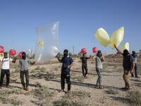 Palestinians stand holding inflated balloons and plastic bags attached with incendiary devices to be directed and flown towards Israel, near Rafah along the border between the Gaza Strip and Israel on August 21, 2020. SAID KHATIB / AFP