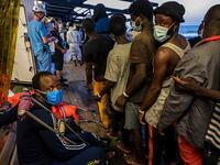 Migrants who have just been helped off the Louise Michel queue to see crew members and doctors including an injured man with crutches (AFP)