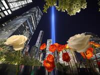 Roses are seen on the 9/11 Memorial as the Tribute in Light art installation shines into the sky over Manhattan on September 11, 2020 in New York to mark the 19th anniversary of the 9/11 attacks. TIMOTHY A. CLARY / AFP