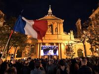 An attendee waves a French flag as people gather on the Place de la Sorbonne in Paris on October 21, 2020, to watch a live broadcast on a giant screen of a national homage at the Sorbonne University to French teacher Samuel Paty, who was beheaded for showing cartoons of the Prophet Mohamed in his civics class. Bertrand GUAY / AFP