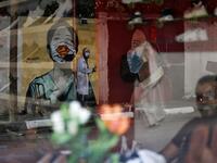The image of a Palestinian student painting a large mural of a mask-clad girl is reflected on the window of a cafe in Gaza City on October 22, 2020, amid the novel coronavirus pandemic crises. Mohammed ABED / AFP