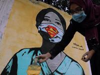 The image of a Palestinian student painting a large mural of a mask-clad girl is reflected on the doors of a shop in Gaza City on October 22, 2020, amid the novel coronavirus pandemic crises. (Instagram)
