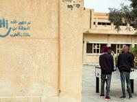 Youths play table football (foosball) outside by abandoned buildings, with graffiti nearby reading in Arabic "this zone has been cleared of the remains of war", in the city of Tawergha, some 200 kilometres (125 miles) east of Libya's capital close to the port city of Misrata, on December 12, 2020. When Libyan dictator Moamer Kadhafi was toppled, people took revenge on those they saw as his supporters -- including the entire town of Tawergha, whose 40,000 residents were forced to flee. Now, almost a decade l