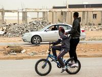 A boy rides behind another on a bicycle along a road past destroyed buildings in the city of Tawergha, some 200 kilometres (125 miles) east of Libya's capital close to the port city of Misrata, on December 12, 2020. When Libyan dictator Moamer Kadhafi was toppled, people took revenge on those they saw as his supporters -- including the entire town of Tawergha, whose 40,000 residents were forced to flee. Now, almost a decade later since militia forces rampaged through the town torching homes, destroying buil