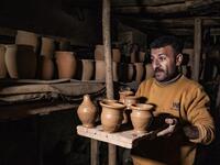 The son of Syrian-Armenian potter Misak Antranik Petros carries vases for drying at his father's workshop located inside an ancient mud-brick house near the city of Qamishli in Syria's northeastern Hasakeh province, on December 19, 2020. Petros was only a teenager when he had to take over for his sick father and become the main potter of the family. He has since become a master of the craft, and is keen to pass his skills on.  Delil SOULEIMAN / AFP