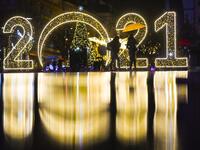 Women walk under an umbrella in front of a 2021 sign displayed in downtown Pristina on December 30, 2020, as Kosovars prepare to celebrate the New Year 2021 at their homes, amid the ongoing Covid-19 (novel coronavirus) pandemic. Armend NIMANI / AFP
