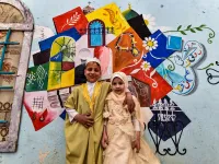 Children pose for a photo in front of a large graffiti depicting cultural elements including mosques