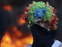 A man wears a face cover and a colorful wig as Palestinians burn tires during a night demonstration the expansion of the Jewish settlement outpost of Eviatar on the lands of Beita village, near the occupied West Bank city of Nablus