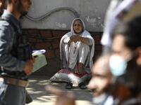 A woman sits as others queue to submit their passport applications at an office in Kabul on July 25, 2021. Dozens begin lining up at the passport office in Kabul before dawn most days, and by eight in the morning the queue already stretches for a good hundred metres. 