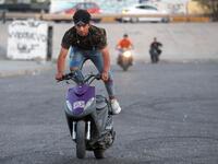 Iraqi youths perform stunts on their scooters in the Jadriya district of Baghdad on August 6, 2021. All dressed up and nowhere to go: many young Iraqis in Baghdad make an effort to be hip, even as they admit their country may have no future. 