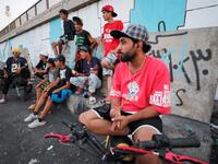 Iraqi youths watch others perform stunts on motorbikes and scooters in the Jadriya district of Baghdad on August 6, 2021. All dressed up and nowhere to go: many young Iraqis in Baghdad make an effort to be hip, even as they admit their country may have no future. 