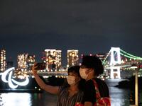 This picture taken on August 21, 2021 shows people taking pictures before the Paralympic Games symbol lit up at night on the Odaiba waterfront in Tokyo. 