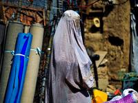 CORRECTION / A burqa-clad woman walks past a stall selling secondhand items at a market in Kandahar on September 22, 2021. 