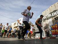 Participants run past Banksy's "The Walled-Off Hotel" near Israel's controversial separation barrier, which divides the West Bank from Jerusalem, in the biblical town of Bethlehem during the 6th International Palestine Marathon on Mar. 23, 2018. 
(Musa AL SHAER / AFP)