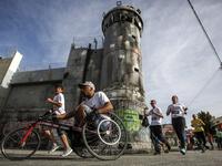 A participant rides in a wheelchair with others running along Israel's controversial separation barrier, which divides the West Bank from Jerusalem, in the biblical town of Bethlehem during the 6th International Palestine Marathon on Mar. 23, 2018. 
(Musa AL SHAER / AFP)