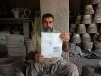 In this photo taken on October 10, 2018.Afghan potter Shirin Agha, 45, poses for a picture as he holds his id card or Tazkira registered to vote in the upcoming parliamentary election at his workshop, on the outskirts of Jalalabad. 
NOORULLAH SHIRZADA / AFP