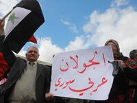 Protesters hold a national flag and a placard in the town of Quneitra in the Syrian occupied Golan Heights, during a demonstration against the US decision to recognise Israel's sovereignty over the Israeli-annexed Golan Heights, on March 26, 2019. The placard reads in Arabic: "The Golan is Arab and Syrian". 
Louai Beshara / AFP