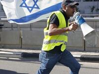 An Israeli protester wearing a yellow vest and carrying a national flag use a loudspeaker to shout slogans during demonstrations against the rising cost of living on December 14, 2018.
JACK GUEZ / AFP