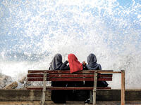 Three Palestinian women sit in the spray from the sea in Gaza City. 