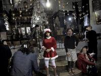 A Palestinian girl dressed in a Santa Claus attire poses alongside other worshippers inside the Church of the Nativity in the West Bank city of Bethlehem, as Christian flock to the what they believe is the birth place of Jesus Christ to celebrate his birth during Christmas mass.
