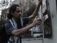 An Egyptian man spraying a graffiti paint on the the wall.