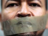 رجل يضع شريطاً لاصقاً على فمه في مظاهرة بألمانيا احتجاجاً على احتجاز الصحفي بقناة الجزيرة، أحمد منصور، من قبل السلطات الألمانية، وذلك بناءً على طلب من الحكومة المصرية، حيث تم الإفراج عنه في وقت لاحق.