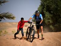 A boy pushes a participant's bike over a sand dune during the Stage 1 of the 14th edition of Titan Desert 2019 mountain biking race around Merzouga in Morocco on April 28, 2019.  FRANCK FIFE / AFP