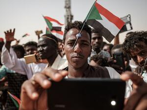 A man poses for a "selfie" photo with a cell phone while having a miniature Sudanese flag placed on his forehead with a plastic suction cap as he awaits the arrival of the deputy head of Sudan's ruling Transitional Military Council. (AFP/ File Photo)