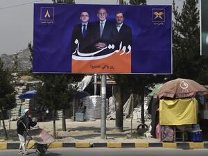 A local residents pushes a wheelbarrow past a billboard with a poster of Afghan presidential candidate and incumbent President of Afghanistan Ashraf Ghani (C) is seen during the first day of the presidential election campaign in Kabul (AFP)