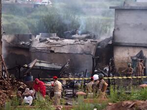 Residents sit among the rubble of their destroyed house as soldiers cordon off the site where a Pakistani Army Aviation Corps aircraft crashed (AFP)