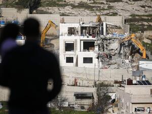 A Palestinian holds a child as he watches Israeli hydraulic shovels demolishing a Palestinian building, north of the occupied West Bank city of Hebron on 14 February 2018 (AFP)