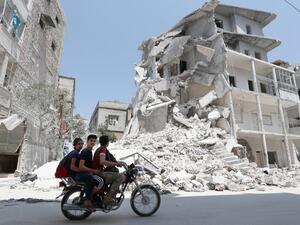 A Syrian man drives a motorcycle past destroyed buildings in the town of Ariha, in the south of Syria's Idlib province (AFP)