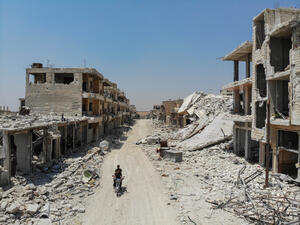 Syrian men riding a motorcycle past the rubble of destroyed buildings in the town of Khan Sheikhun in the southern countryside of Idlib. (AFP/ File Photo)