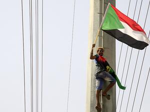 A Sudanese demonstrater waves his national flag in front of the Algerian embassy as people celebrate in Khartoum (AFP)