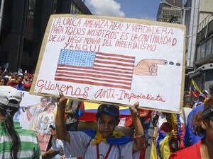 Holding up a sign with a slogan against US, a pro-government protester participates in a demonstration against US sanctions in Caracas on August 7, 2019. (AFP/ File Photo)